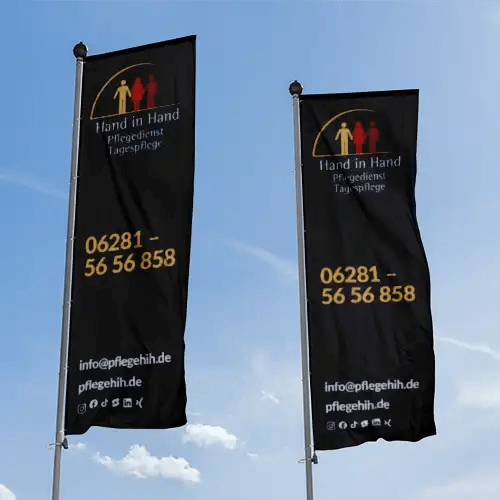 PS Midia – Beispiel Werbetechnik: zwei bedruckte Fahnen des Pflegedienstes Hand in Hand vor blauem Himmel.